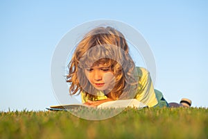 Kid read book in park. Child boy reading book laying on grass on grass and sky background with copy space outdoor.