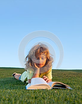 Kid read book in park on green grass lawn.