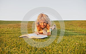 Kid read book in park. Smiling funny child in t-shirt having fun reading book in park.