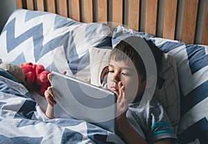 Kid reading bed time stories on tablet before sleep, Happy boy sitting in bed playing games on digital pad, Child relaxing at home