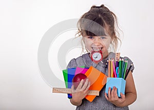 Kid ready for school. Cute clever child in eyeglasses holding school supplies: pens, notebooks, scissors, alarm clock and apple.