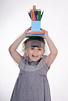 Kid ready for school. Cute clever child holding school supplies: pens, notebooks, scissors on her head.