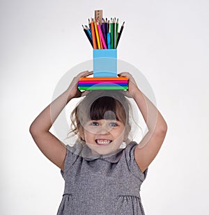 Kid ready for school. Cute clever child holding school supplies: pens, notebooks, scissors on her head.