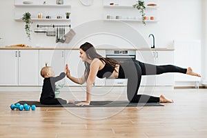Kid responding to high-five gesture from mom on yoga mat