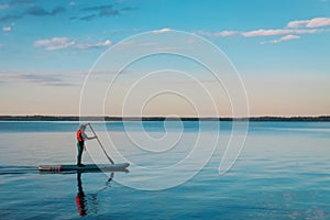 Kid riding on paddle sup surfboard in water at sunset