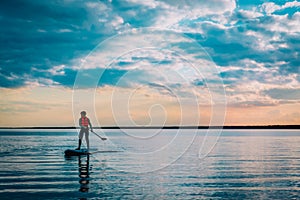 Kid riding on paddle sup surfboard in water at sunset