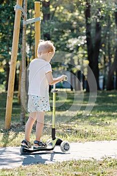 Kid with riding scooter in summer park