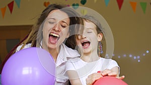 Kid`s birthday party . Little cute girl is celebrating her b-day with young mother with dreadlocks inflating the