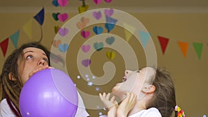Kid`s birthday party . Little cute girl is celebrating her b-day with young mother with dreadlocks inflating the