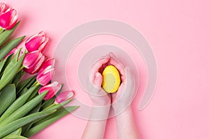 Kid`s hands holds easter egg. Easter holiday background with pink flowers tulips and free copy space. Flat lay.