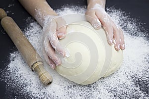 Kid`s hands, some flour, wheat dough and rolling pin on the black table. Children hands making the rye dough for backing bread.