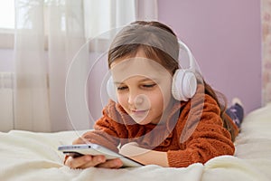 Kid\'s internet content. Caucasian little girl playing on smartphone using mobile app listening music with headset