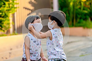 Kid in safety wearing mask in town. Twin Children wearing medical face mask outdoor. Twin Child  helps to put a mask on his face t