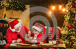 Kid Santa Claus enjoying in served gingerbread cake and milk. Santa Father and son having fun near Christmas tree and