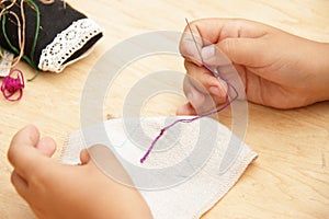 Kid is sewing, making ebroidery on natural fabric