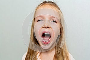 Kid showing the first milk tooth. Change teeth concept. Cute little girl with blonde hair on gray background with copy space