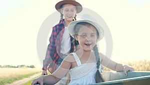 Kid sisters children play with a garden trolley car ride on wheelbarrow. Little girl child in hat happy family