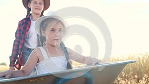 Kid sisters children play with a garden trolley car ride on wheelbarrow. little girl lifestyle child in hat happy family