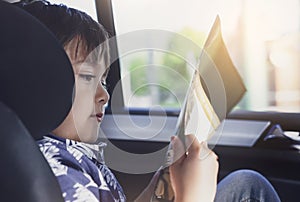 Kid siting on car seat and reading a book, Little boy sitting in the car in child safety seat, Portrait of toddler entertaining