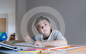 Kid siting on table doing art and craft for school homework, Child boy holding colour pen drawing or painting on white paper,