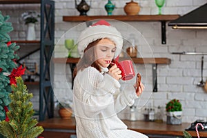 Kid sitting in Christmas decorated cozy kitchen and wearing red santa claus hat