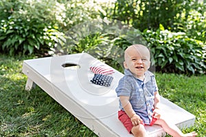 Kid sitting on Corn hole board in backyard on fourth of July