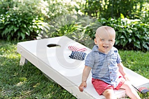 Kid sitting on Cornhole board in backyard on fourth of July