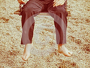 Kid sitting with feet against a sand in summer playground