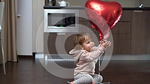 Kid sitting on the floor with a big balloon heart, child on Valentine's Day, toodler playing with foil balloon alone