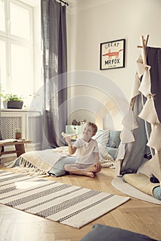 Kid sitting on the floor with toy airplane in natural playroom with comfortable bed and scandinavian tent, real photo