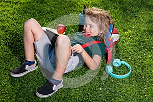 Kid sitting on grass with tablet in the park. Outdoor school. Smiling boy hold tablet computer. School, education