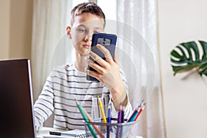 Kid sitting with laptop computer and scrolling phone instead of doing homework at home