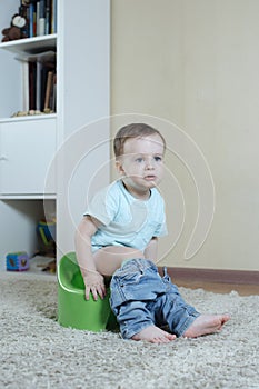 The kid is sitting on a pot with jeans down and is unhappy with something