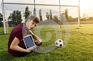 Kid sitting on soccer pitch , holding tablet and pointing to it