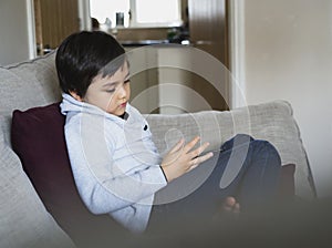 Kid sitting on sofa watching cartoon on tablet, Sad child sitting alone looking down deep in thought, Boy relaxing at home playing