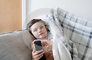 Kid sitting on sofa watching TV, A boy holding remote control and looking up with smiling face, Positive child lying on sofa enjoy