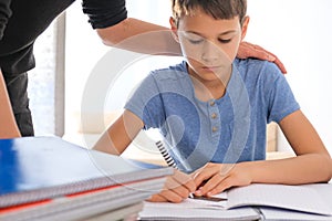 Kid sitting at the table with many books notebooks and doing homework. Mother helping him. Learning difficulties