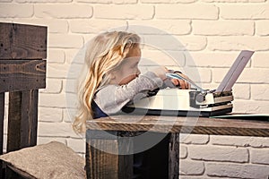 Kid sitting at table and typing typewriter with paper