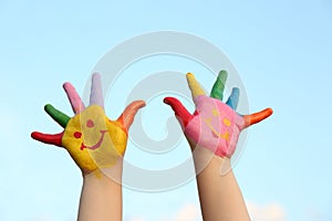 Kid with smiling face drawn on palms against sky, closeup