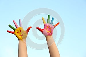 Kid with smiling face drawn on palms against sky, closeup. School holidays