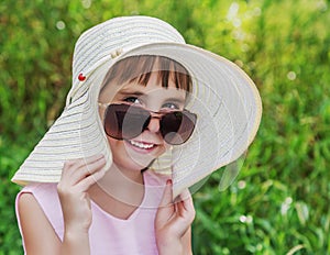 Kid smiling in sunglasses and a hat.