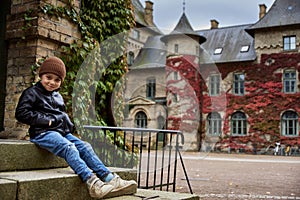 Kid smiling by a Swedish old university in a castle with red ivy climbing a brick wall in Autumn. Child sitting by campus entrance