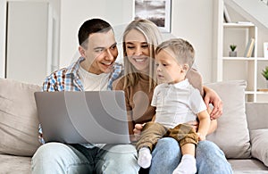 Kid son learning computer doing online shopping sitting with parents on couch.