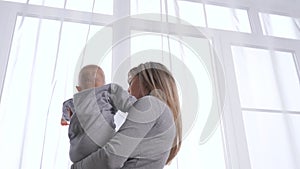 Kid son and young mom are playing looking out the window together waiting for dad. Happy family. Mother, child, daughter