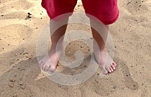 Kid standing bare footed on the sand in red shorts. Child`s feet with cute toes, happy feeling, warm sumer day, Earth day