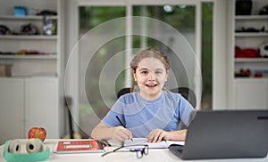 Kid studying at home with laptop and books. Child study online using laptop at desk. Studying with homework in child room. E