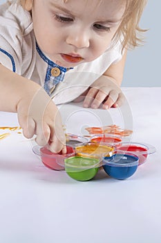 The kid stuffed his finger in the paint on the palette. The child`s hand is smeared with paint