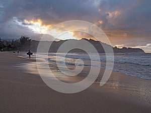 Kid surfer holding bodyboard leaving ocean at sunset