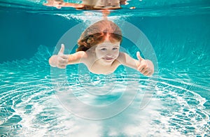 Kid swim underwater in pool. Child boy swimming under water with thumbs up.