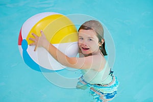 Kid in swimming pool play with inflatable ball. Happy child having fun on summer vacation. Kid playing with ball in the